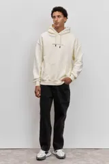 Buzo con capucha de corte holgado, color crema, con bolsillo frontal tipo canguro y pequeña estampa tipográfica en el pecho.