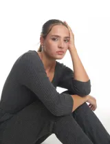 Enterito de tejido de punto con textura canalé, color gris oscuro. Presenta escote redondo, mangas tres cuartos y cintura elastizada con lazo de ajuste. La parte inferior tiene un calce relajado tipo jogger con puños elastizados y bolsillos laterales.