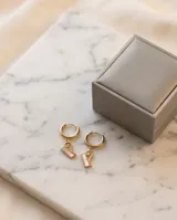 Caravanas de acero dorado con argolla pequeña y dije colgante en forma de barrita geométrica con detalle de espiral.