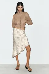 Falda midi de tejido satinado con estampado de lunares, tiro medio, cintura elástica y bajo asimétrico.