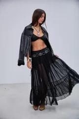 Pollera larga de microtul transparente, color negro, con diseño fluido y volados en el ruedo. Cuenta con una cintura elástica adornada con tachas circulares metálicas.