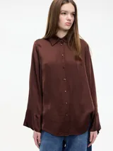 Camisa de corte amplio y fluido, confeccionada en viscosa con acabado satinado. Presenta cuello clásico, cierre frontal con botones y mangas largas con puños acampanados.
