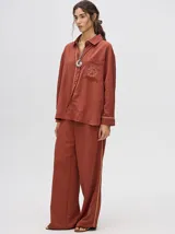 Pantalón de corte holgado y tiro alto con caída recta, color azul petróleo. Presenta una franja lateral decorativa en tonos rojo y amarillo que recorre la pierna, a juego con la camisa de la misma línea.