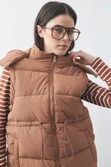 Chaleco puffer negro con diseño acolchado, capucha desmontable y cierre frontal. Cuenta con cordones ajustables en la cintura y bolsillos laterales.