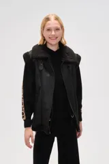 Chaleco de estilo aviador en color marrón, confeccionado en material tipo cuero con interior y bordes de corderito sintético en color crema. Presenta cierre frontal, cuello alto con tira de ajuste y bolsillos laterales.