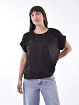Blusa negra de manga corta con cuello redondo. La parte superior del pecho y los hombros están confeccionados en tela de encaje calado con diseño geométrico, mientras que el cuerpo es de tela lisa.