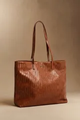Cartera tipo tote bag color marrón whisky, con diseño trenzado y tiras largas para el hombro. Incluye placa metálica con el logo de la marca.
