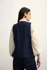 Chaleco azul de denim con cuello en V y cierre frontal con botones metálicos. Posee bolsillos delanteros y corte clásico.