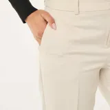 Pantalón de vestir corte pitillo en color beige, con diseño liso, cierre frontal y bolsillos laterales.