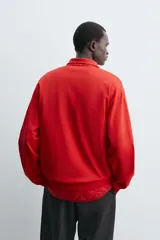 Sudadera de algodón ligero en color rojo, con cuello subido y cierre frontal de cremallera. Presenta mangas largas con puños acanalados y dobladillo inferior en rib.