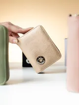 Monedero de cuero sintético con textura granulada en color dorado, con cierre perimetral y aplique metálico circular con logo grabado en el frente.