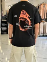 Remera oversize negra con estampa gráfica en la espalda que incluye un tiburón naranja, texto tipográfico y detalles en blanco.