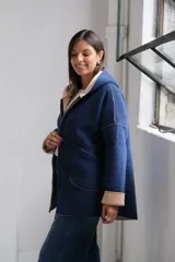 Tapado de paño azul marino con capucha, cierre frontal y detalles en color beige en el interior de la capucha, puños y bordes. Presenta bolsillos frontales aplicados y costuras visibles.