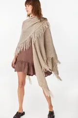 Ruana de punto color beige con diseño abierto y flecos en los bordes.