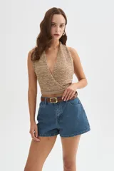 Top de punto con lentejuelas en tonos beige y dorado, con escote halter cruzado en V, sin mangas y corte corto.