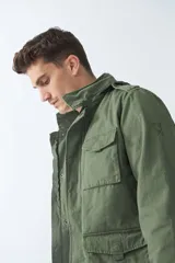 Campera de gabardina verde militar con capucha desmontable y ajustable, cierre frontal con cremallera y múltiples bolsillos con solapa.