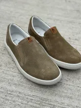 Zapato slip-on verde oscuro de gamuza con perforaciones, suela blanca y elástico lateral.