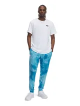 Pantalón de jogging Under Armour con estampado tie-dye en tonos azules. Presenta cintura elástica con cordón ajustable, bolsillos laterales y puños elásticos en los tobillos. Incluye el logo de la marca bordado en la parte superior derecha.