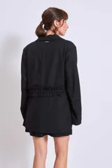 Blazer negro con solapas de muesca, corte holgado, cierre frontal con lazo y detalle de volados en los bolsillos.