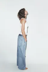 Jeans de tiro medio, color azul claro, con doble cinturilla y trabillas. Presenta cinco bolsillos, detalles de rotos y cierre frontal con cremallera y botones.