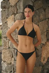 Conjunto de bikini color negro confeccionado en lycra mate. El corpiño es de estilo triangular con breteles ajustables y detalles metálicos. La bombacha es de corte vedetina con laterales ajustables mediante tiras y detalles metálicos en los extremos.