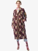 Saco largo de corte recto con estampado floral sobre base color bordó. Presenta cierre frontal con botones, cuello camisero, bolsillos laterales y un parche bordado decorativo en la manga izquierda. Incluye un forro interior desmontable acolchado.