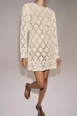 Vestido corto de punto calado en color crudo, con cuello redondo, manga larga y detalles de abalorios aplicados en forma de lentejuelas y flores.