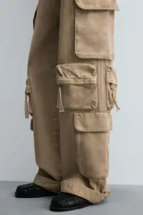 Pantalón cargo de denim lavado negro, corte relajado y tiro medio. Presenta múltiples bolsillos cargo con solapa y detalle de cierre en las perneras, además de bolsillos de vivo traseros. El bajo es ajustable con trabilla.