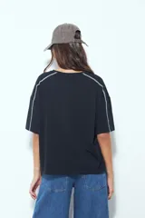 Remera de manga corta con silueta relajada y costuras a la vista en color blanco que contrastan sobre el tejido negro. Presenta un diseño moderno con terminaciones destacadas.