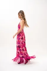 Vestido largo fucsia con estampado abstracto en tonos rosados y morados, cuello halter cruzado y flecos largos en el dobladillo inferior.