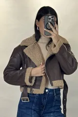 Campera tipo aviador de cuero sintético marrón con interior y detalles de corderito beige. Presenta cierre frontal cruzado, cuello solapa amplio, puños con corderito y cinturón ajustable en la cintura con hebilla metálica.