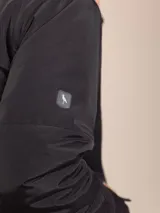 Campera negra con capucha, cierre frontal con cremallera y bolsillos laterales con botón a presión.