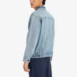 Chaqueta de denim de corte holgado, lavado medio, con bolsillos frontales con solapa, cierre de botones metálicos y detalles de parches e impresiones en tonos más oscuros.