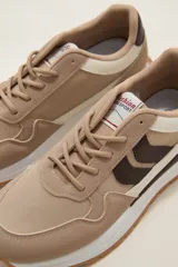 Zapatilla deportiva de diseño urbano, combinando paneles de tela blanca y gamuza sintética en tono gris claro. Cuenta con cordones grises, suela de plataforma con entresuela blanca y base dentada en color caramelo.