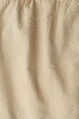 Pantalón de sirsaca de algodón color beige, con cintura elástica y cordón ajustable, cierre con botón, bolsillos laterales y bolsillos traseros insertados. Corte relajado.
