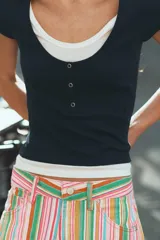Camiseta efecto doble en color crudo y blanco, de manga corta y corte slim fit. Cuenta con escote redondo, cierre frontal parcial con botones a presión y diseño de capas superpuestas.