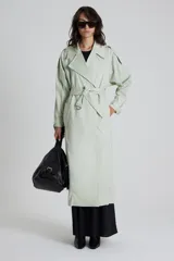 Trench color verde claro con cuello solapa, doble botonadura, cinturón y bolsillos laterales.
