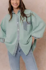 Camisa de denim color verde menta con calce relajado, cuello clásico, cierre frontal con broches metálicos, mangas largas y bolsillo aplicado en el pecho, con detalles en tono gris azulado a contraste en cuello, cartera, bolsillo y puños.