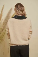 Saco de punto color beige con cuello, puños y detalle de bolsillo en color negro. Presenta cierre frontal con botones dorados y diseño de corte holgado.
