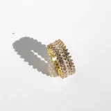Anillo dorado con tres hileras de cristales blancos de diferentes tamaños.