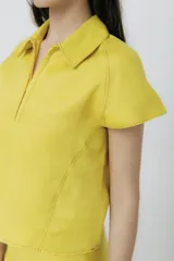 Top de lino color blanco, con cuello polo, cierre frontal parcial y mangas cortas. Presenta pespuntes a contratono.