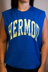 Musculosa de corte boxy, color azul vibrante, con cuello redondo y sisas amplias. Estampado frontal arqueado con la palabra "HERMOD" en tipografía universitaria desgastada color amarillo claro.