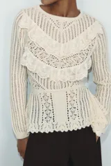 Jersey de punto color crudo con cuello redondo y manga larga. Presenta un diseño calado con detalles de encaje en el frente y un bajo asimétrico.