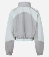 Campera corta viento de mujer de la marca Blue Steel, con cuello alto, mangas largas con puños elásticos y cierre frontal por cremallera. Presenta recortes contrastantes en tonos gris, celeste y amarillo pastel, y ruedo corto con elástico. Confeccionada en poliamida, un tejido sintético ligero y suave.