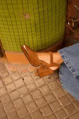 Sandalia de gamuza color marrón, con taco ancho, punta fina y tira ajustable al tobillo. Incluye detalle metálico en la puntera.