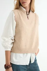 Chaleco tejido de punto color verde salvia, con cuello redondo y diseño sin mangas. Presenta detalles de pequeños apliques brillantes distribuidos por toda la prenda.