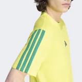 Remera Adidas de algodón color amarillo, con cuello redondo y mangas cortas. Presenta el logo de la marca bordado en el centro del pecho y las icónicas tres rayas de la marca en color verde sobre los hombros y mangas.