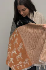 Pashmina de textura suave con diseño patchwork que combina estampados de caballos y patrones de líneas en zigzag. Presenta una paleta de colores en tonos naranja, negro y beige.