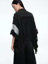 Camisa de corte oversize en color crudo, confeccionada con una mezcla de texturas que incluye paneles de encaje, detalles bordados y aplicaciones de tachas metálicas. Presenta mangas amplias tipo murciélago, cuello clásico y cierre frontal con botones.