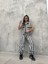Chaleco de denim sin mangas, con cuello mao y cierre frontal con botones. Presenta bolsillos ojal en el pecho con solapa y un diseño a rayas verticales en tonos rosados y blancos con efecto desteñido.